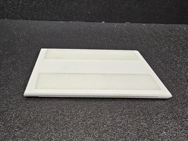 Rectangular white Spacer Attachment (D) with two recessed sections, placed on a dark, textured surface.