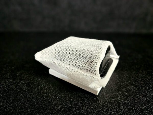 A small rectangular object covered in a white mesh-like material, FF-5 for 5/8″ (1.58 CM) TO 1-1/4″ (3.2 CM), rests on a black surface.