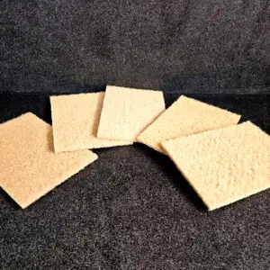 Five rectangular, beige *Scrub Pad (A)* are arranged in a fan shape on a dark, textured surface.