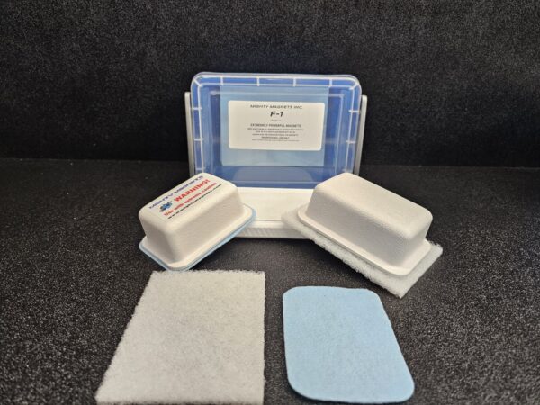 A small plastic container labeled "F-1 for 1/8″ (.32cm) to 1/4″ (64cm)" with two foam pads, two metal blocks, and a blue rectangular pad on a black surface.