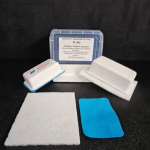 Two white magnets with plastic cases, a white abrasive pad, and a blue cloth lie next to a clear plastic container labeled "F-9 1-3/4″ (4.4 cm) to 2-1/4″ (5.7 cm)" against a black background.
