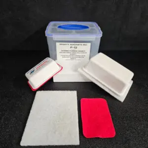 A plastic container labeled "Mighty Magnets Inc. F-9 1-3/4″ (4.4 cm) to 2-1/4″ (5.7 cm)" with a blue lid, surrounded by foam pads and a white cleaning cloth.
