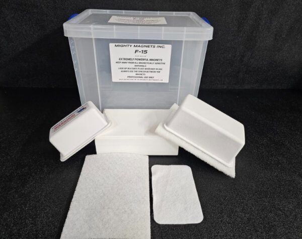 A plastic container labeled "F-9 1-3/4″ (4.4 cm) to 2-1/4″ (5.7 cm)" from "Mighty Magnets Inc." is surrounded by several white pads and a small white box with a lid. The background is black.