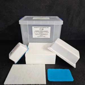 A plastic storage box labeled "F-9 1-3/4″ (4.4 cm) to 2-1/4″ (5.7 cm)" is surrounded by white rectangular foam pads, a white scouring pad, and a blue pad on a black surface.