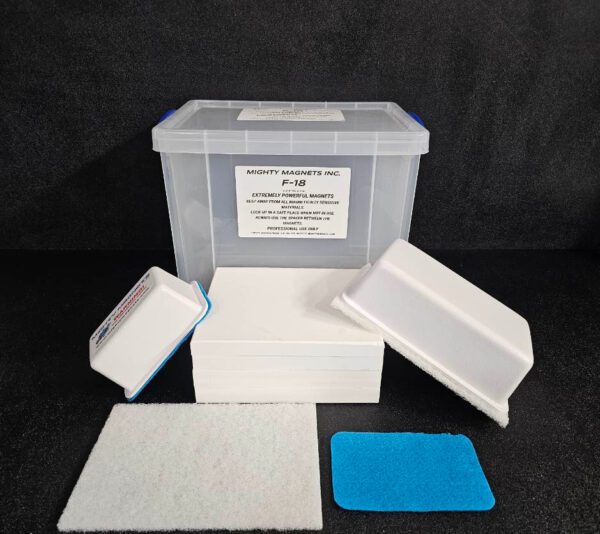 A plastic storage box labeled "F-9 1-3/4″ (4.4 cm) to 2-1/4″ (5.7 cm)" is surrounded by white rectangular foam pads, a white scouring pad, and a blue pad on a black surface.
