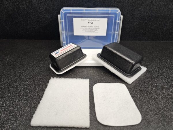 Two rectangular, black magnet covers, a blue-lidded carrying case labeled "F-2 for 1/4″ (.65cm) to 1/2″ (1.27cm)", and two white padding sheets are arranged on a black surface.