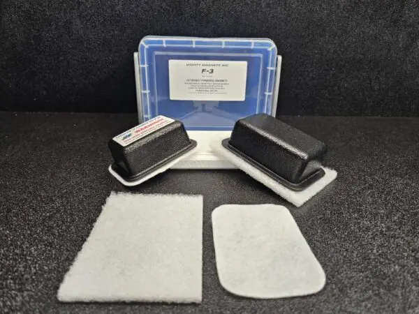 Two rectangular plastic enclosures, a blue and white container labeled "F-2 for 1/4″ (.65cm) to 1/2″ (1.27cm)", and two white felt pads are arranged on a black surface.