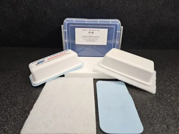 A plastic case labeled "F-4 for 1/2″ (1.3 cm) to 1″ (2.5 cm)" with two white rectangular containers, a white pad, and a blue pad are displayed on a dark surface.