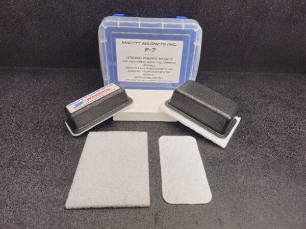 A set of F-6 for 1″ (2.5 cm) to 1-1/2″ (3.8 cm) products includes a labeled plastic container, two black rectangular magnets with padding, and two rectangular fabric pieces on a black surface.