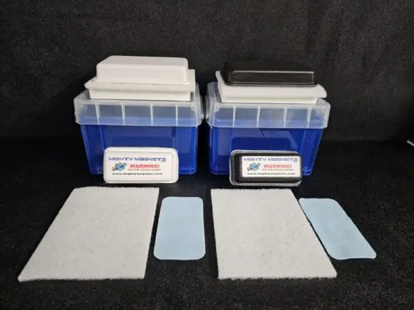 Two plastic containers with attached scrub pads on top, positioned on a dark surface. Each box has additional scrub pads lying in front of them, along with "FF-5 for 5/8″ (1.58 CM) TO 1-1/4″ (3.2 CM)" labels displaying a warning.