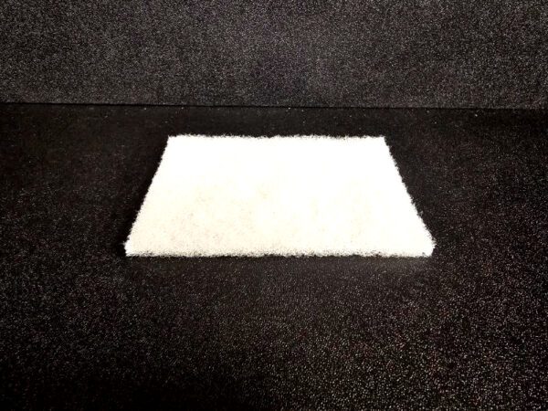 A white rectangular Scrub Pad (A) lies on a black textured surface.